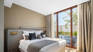 Une chambre moderne avec un grand lit, une tête de lit dotée d’un panneau de commande et une porte-fenêtre coulissante donnant sur un espace extérieur.