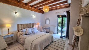 A bedroom with a bed, bedside lamps, a desk, and a view of the outdoors through a glass door. - Quiet cottage with terrace, pets welcomed, near pony farm (Virigneux)