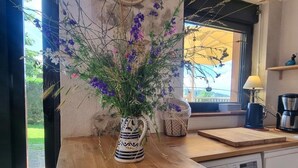 A kitchen with a wooden countertop, a decorative vase with purple flowers, a small figurine, and a window with a view of greenery. - Quiet cottage with terrace, pets welcomed, near pony farm (Virigneux)