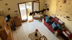 Ein gemütliches Wohnzimmer mit einer Couch, einem Couchtisch und einem Fernseher. Eine Glastür führt in einen Außenbereich.