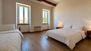 Une chambre avec deux lits, de grandes fenêtres, des poutres en bois et un radiateur.