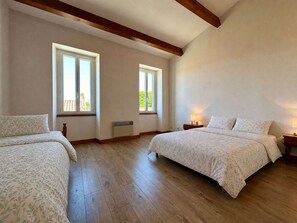 A bedroom with two beds, large windows, wooden beams, and a radiator.