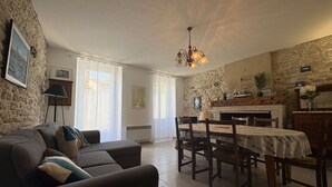 Un salon chaleureux avec un canapé, une table à manger et des chaises. On y trouve une cheminée, un mur en pierre et un lustre.