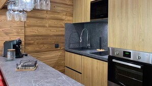 A modern kitchen with wooden cabinets, a black countertop, a Bosch coffee maker, and a stainless steel oven. - Charming renovated studio with balcony and WIFI, near the slopes (Pra-Loup)