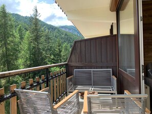 A balcony with a view of a forested mountain, a wooden railing, and a covered seating area with metal chairs. - Charming renovated studio with balcony and WIFI, near the slopes (Pra-Loup)