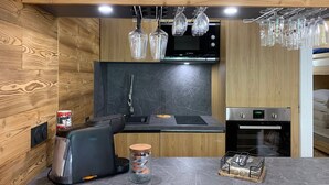 A modern kitchen with wooden panel walls, a Bosch microwave, a sink, and a built-in oven. - Charming renovated studio with balcony and WIFI, near the slopes (Pra-Loup)