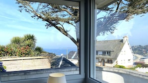 A room with a large window overlooking a coastal town, a lamp, and a cup on the windowsill.