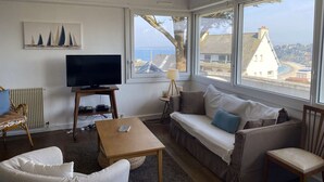 A living room with a TV, sofa, and large windows overlooking a coastal view.