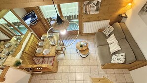 A cozy, well-lit living area with a wooden dining table set for four, a sofa with patterned cushions, and a hanging light fixture. - Mezzanine Studio with Balcony, Near Ski Shuttle & Swimming Lake - Sleeps 6 (Praz-sur-Arly)