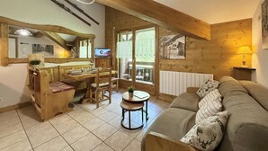 A cozy cabin interior with a wooden dining area, a sofa, and a television. - Mezzanine Studio with Balcony, Near Ski Shuttle & Swimming Lake - Sleeps 6 (Praz-sur-Arly)