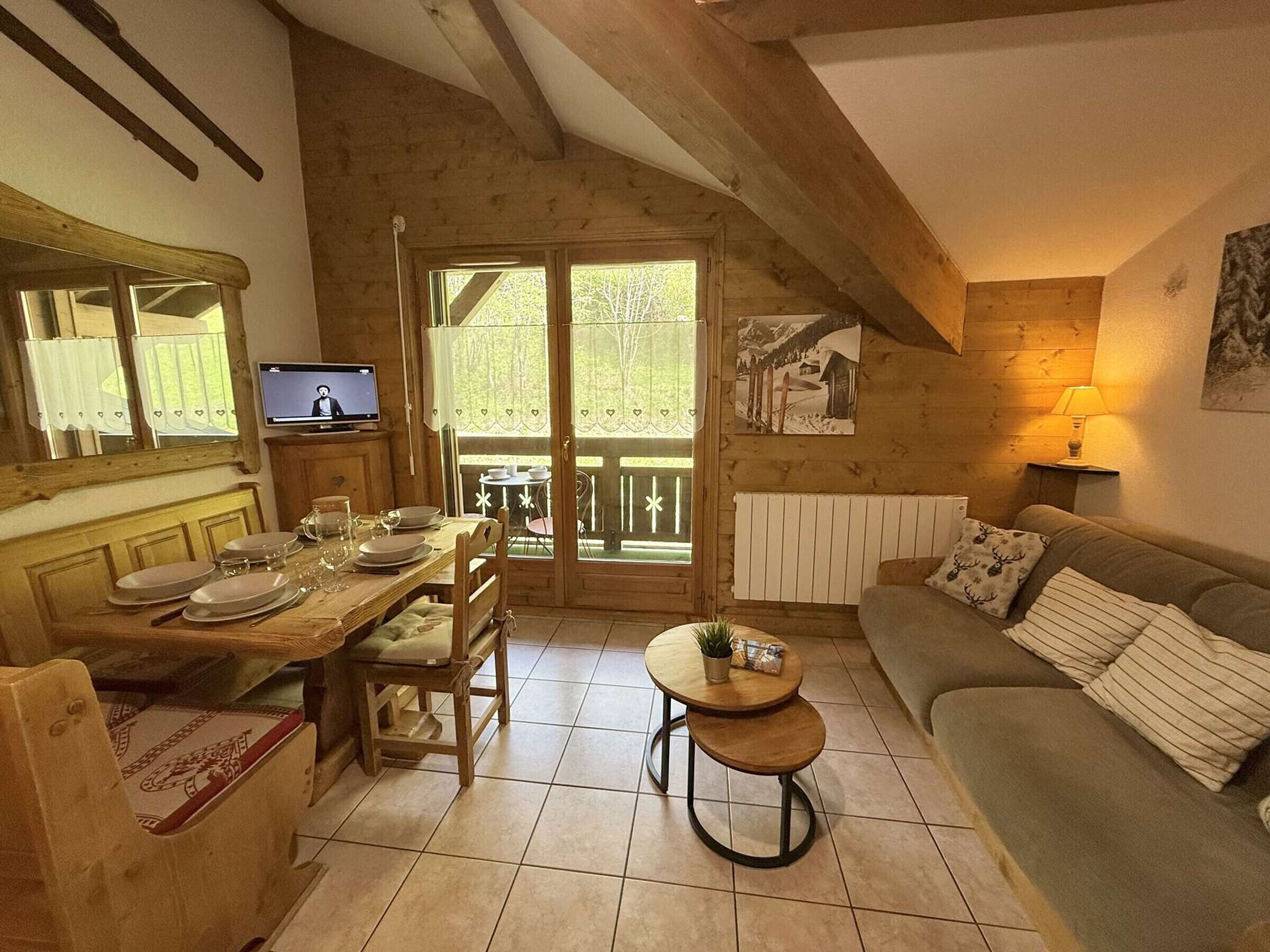 A cozy wooden cabin interior with a dining area, a sofa, and a television.