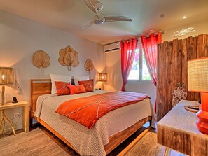 A bedroom with a wooden bed, red curtains, a ceiling fan, wall art, and a desk with a lamp.