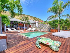 A wooden deck with a pool, lounge chairs, and a decorative turtle sculpture.