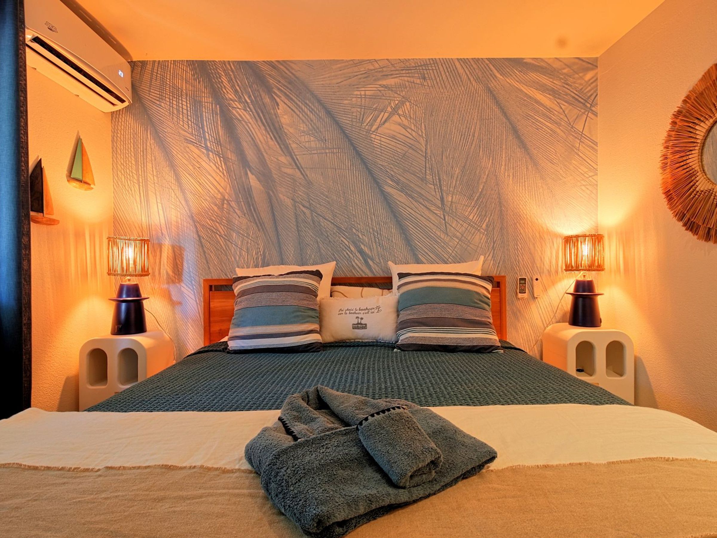 Una camera d'albergo con un letto grande, due lampade ai comodini, un arazzo a parete e un condizionatore d'aria fissato al muro.