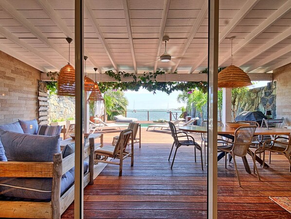 A wooden deck with outdoor seating, a view of the sea, and a stone wall.