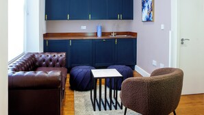 A compact living space with a kitchenette, a brown leather sofa, a small table, and a brown armchair. - Putera Puteri Residence (London)