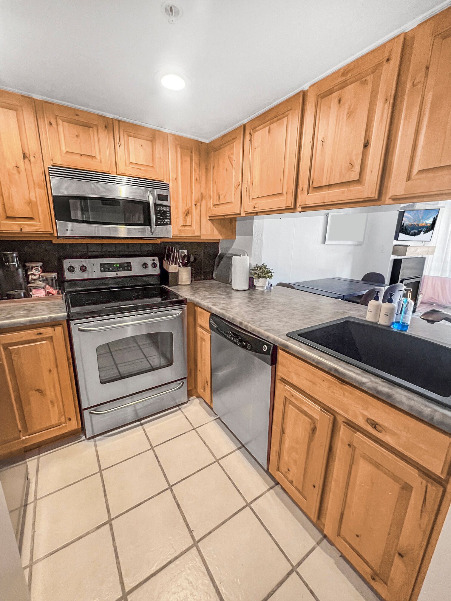 A kitchen with wooden cabinets, stainless steel appliances, a dishwasher, and a tiled floor.
