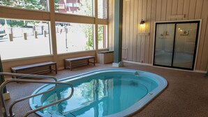 En indendørs swimmingpool med et glasfacade, træbænke og udsigt til det fri gennem store vinduer.