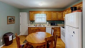 A compact kitchen with wooden cabinets, a dining table, and basic appliances. - Scenic Solitude at Cabins in the Clouds! (Rising Fawn)