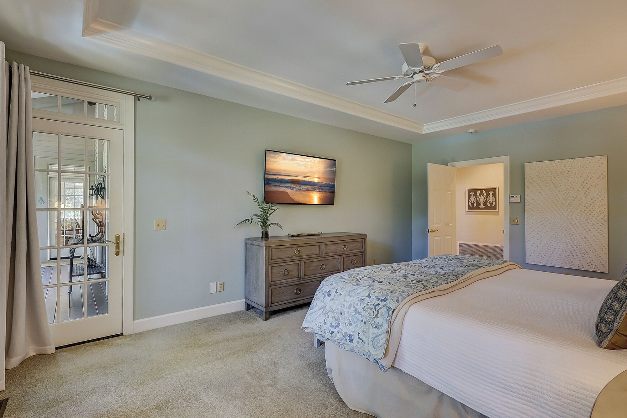 Une chambre à coucher avec un lit, une commode, un ventilateur de plafond, un tableau et une porte.