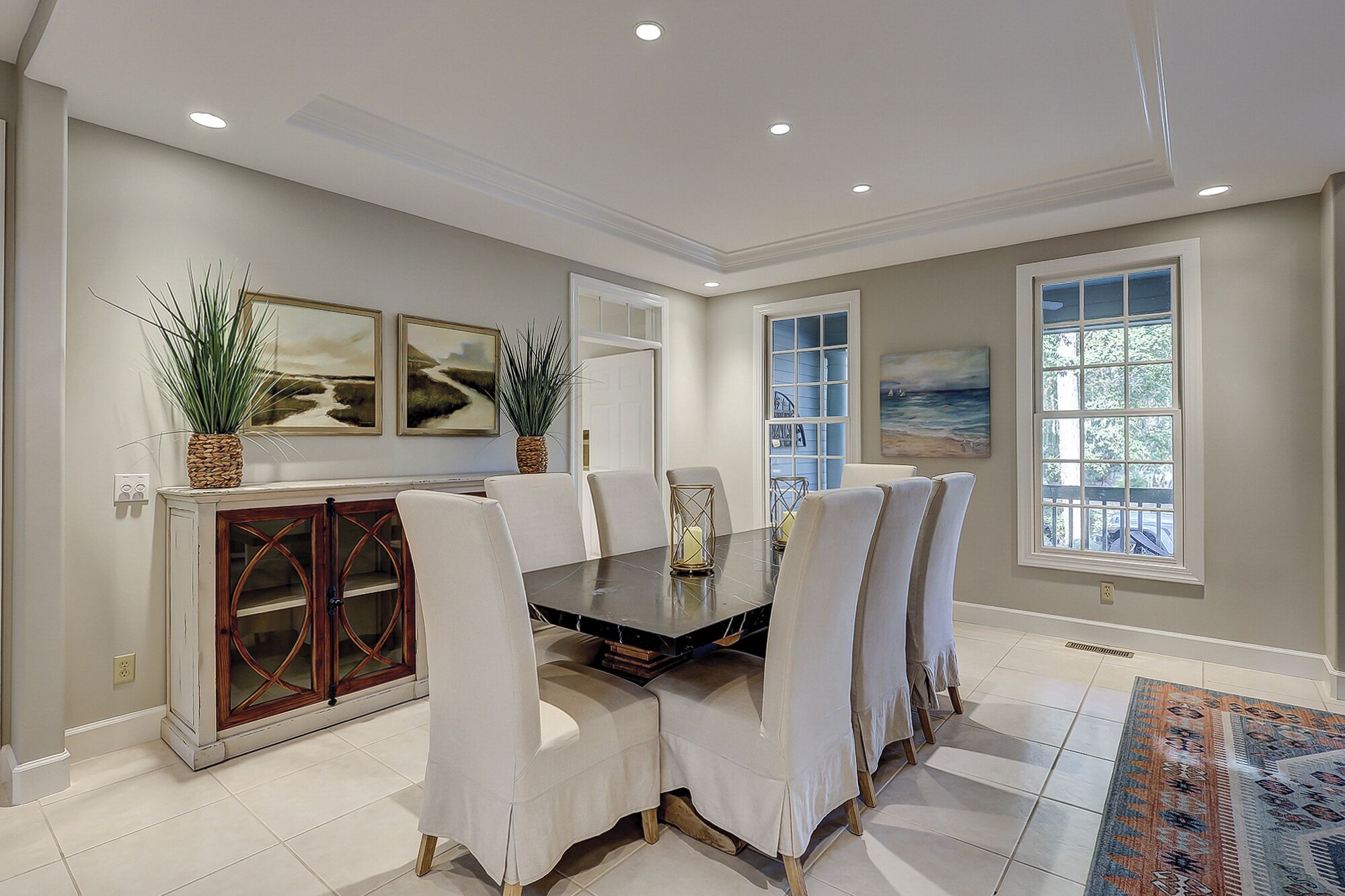 A dining area with a large table, white chairs, a wooden cabinet, and artwork on the walls.