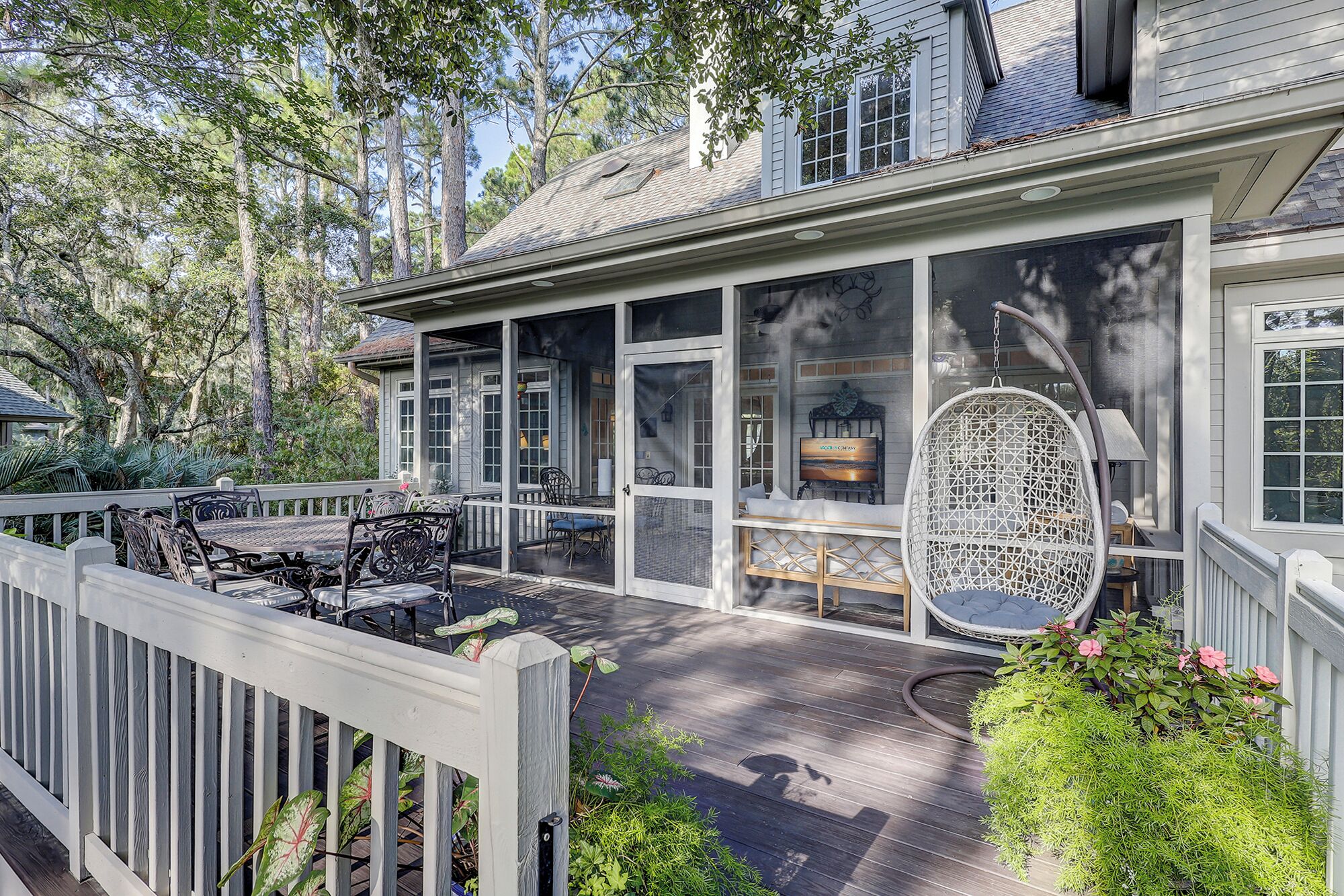 A covered porch with a dining table and chairs, a hanging chair, and a small garden area with plants and flowers.