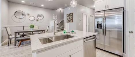 A modern kitchen with white cabinets, a stainless steel refrigerator, and a built-in dishwasher.
