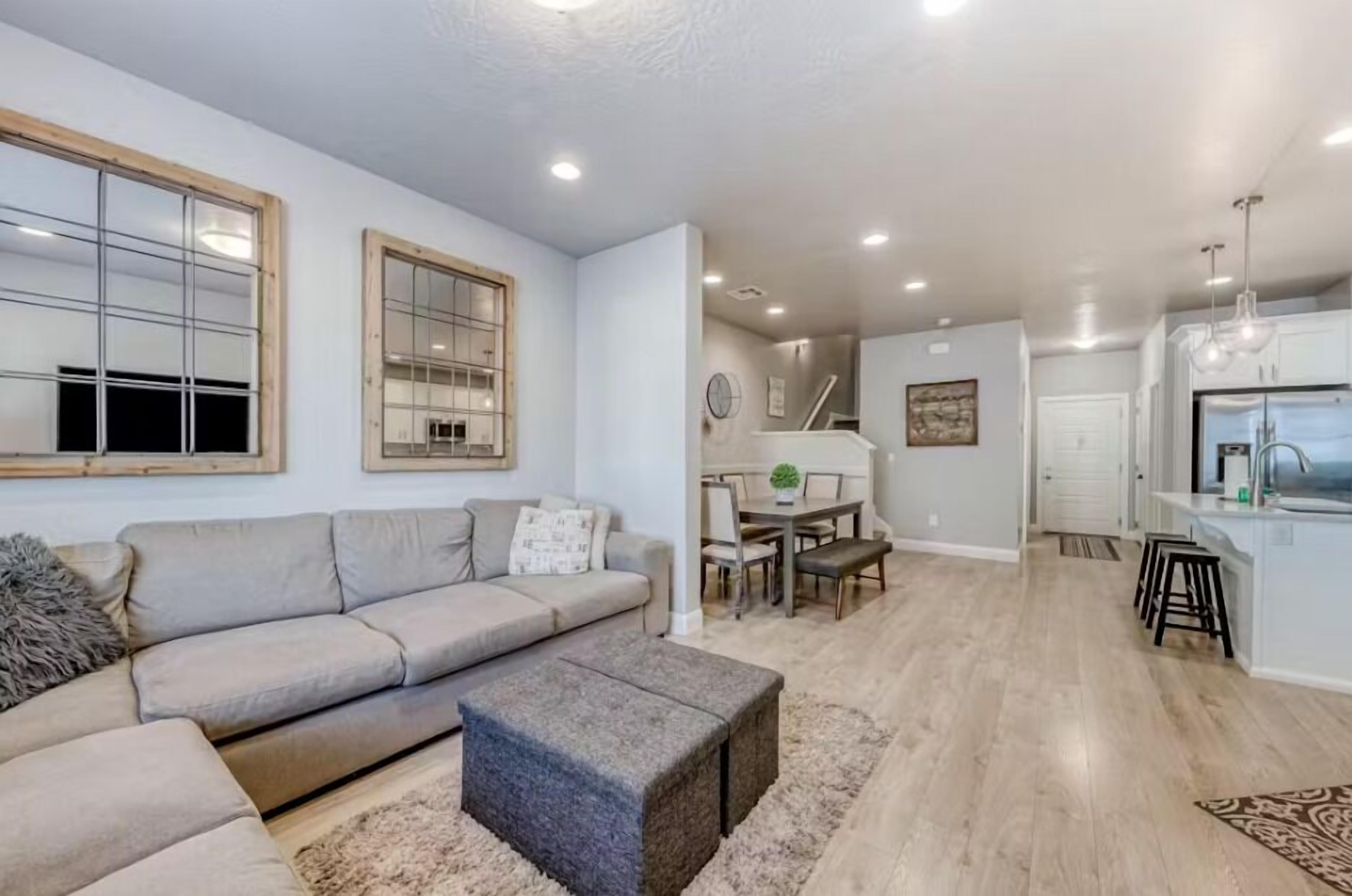 Una sala de estar moderna con sofá, reposapiés y un comedor con mesa y sillas.