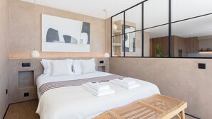 Moderni hotellihuone, jossa on suuri sänky, yöpöytä, peili ja seinälle kiinnitetty taideteos.