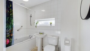 Ein Badezimmer mit Badewanne, Waschbecken, Toilette und einem Fenster mit Pflanzen.