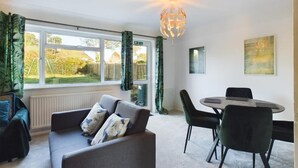 Ein modernes Wohnzimmer mit einer Couch, Sesseln, einem Esstisch und einem großen Fenster mit Vorhängen.