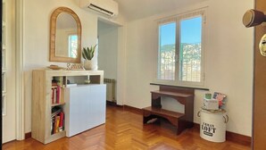 A spacious room with a wooden herringbone floor, a white desk with a computer, a large mirror, and a window with a city view. - Happy Family Apartments Panorama (Genoa)