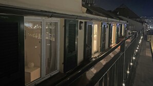 A row of closed hotel rooms with a balcony, a railing, and a view of the city at night. - Happy Family Apartments Panorama (Genoa)