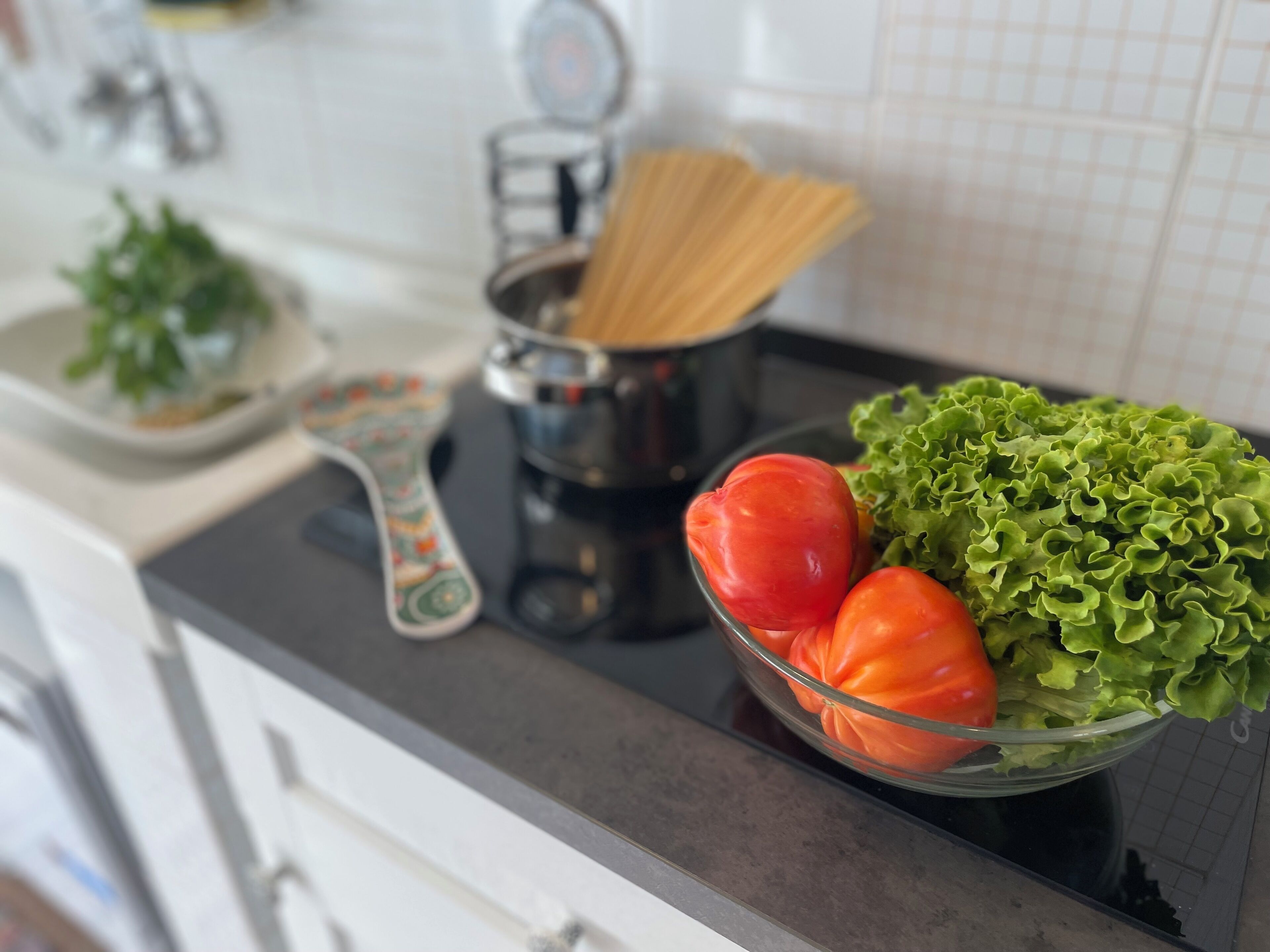 Eine Küchenarbeitsplatte mit einer Schüssel, die Salat und Tomaten, eine Pastamaschine und ein Messbecher enthält.
