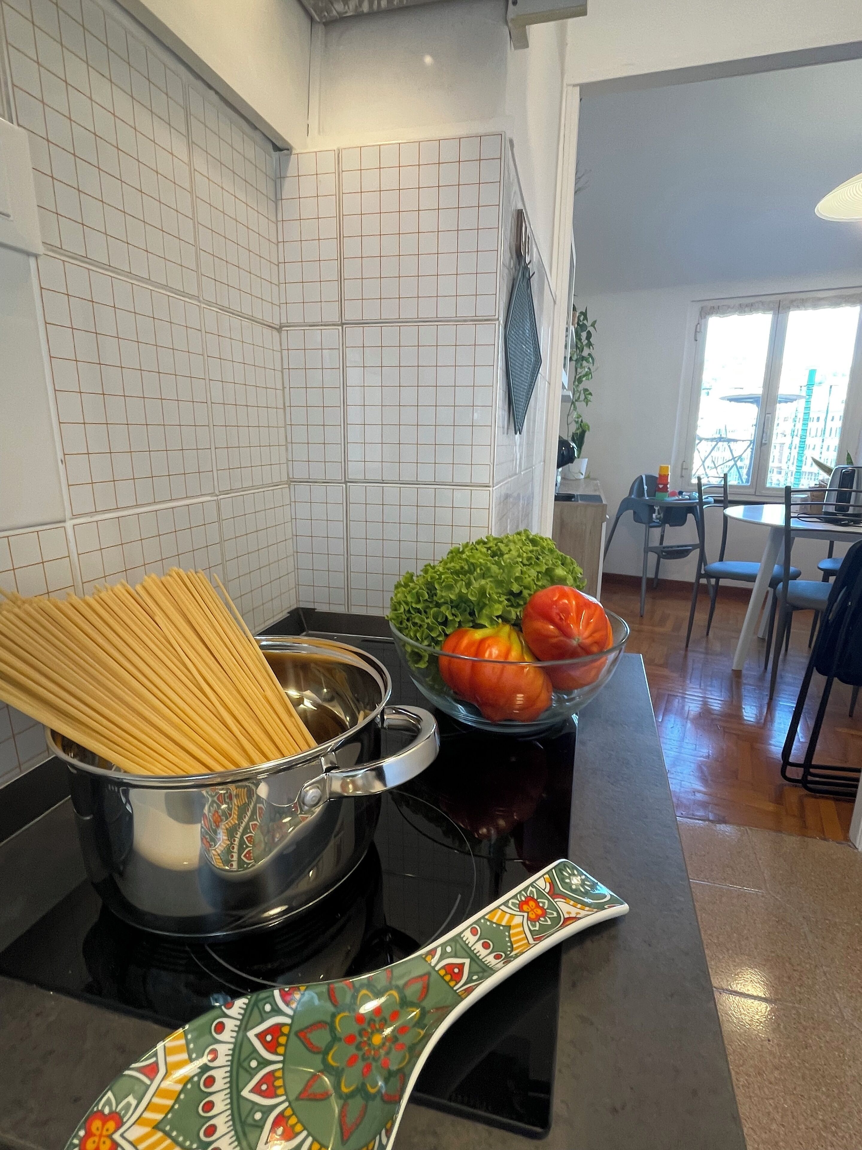 A kitchen with a stove, a pot of spaghetti, a bowl of vegetables, and a colorful backsplash.