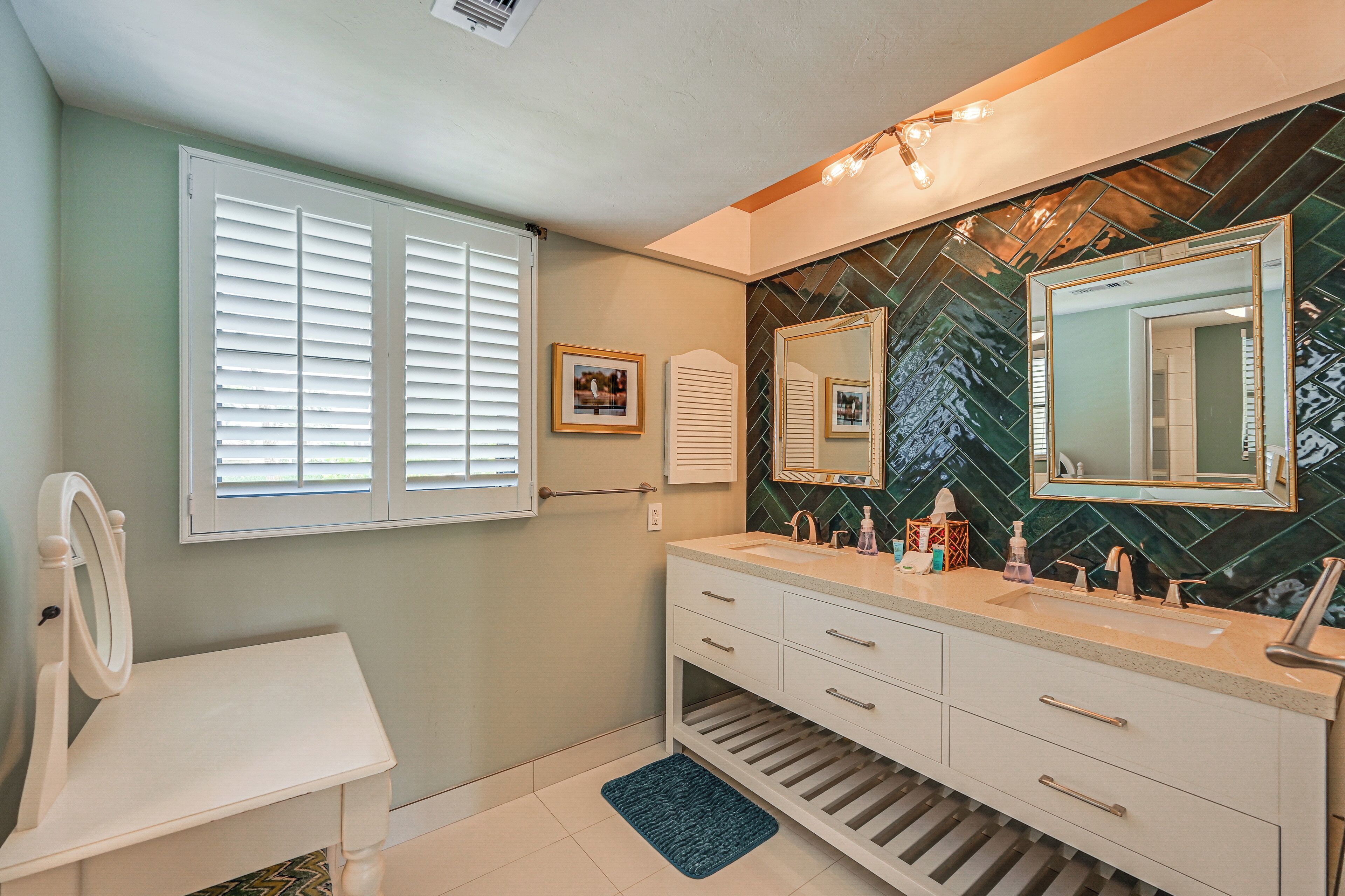 A bathroom with a white vanity, a large mirror, and a green mosaic backsplash.