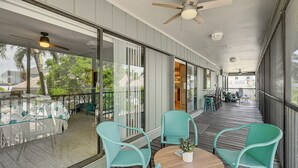 A covered outdoor area with a wooden deck, glass railings, and wicker chairs. - Marco Island Family Home: Pool, Lanai, Backyard! (Marco Island)