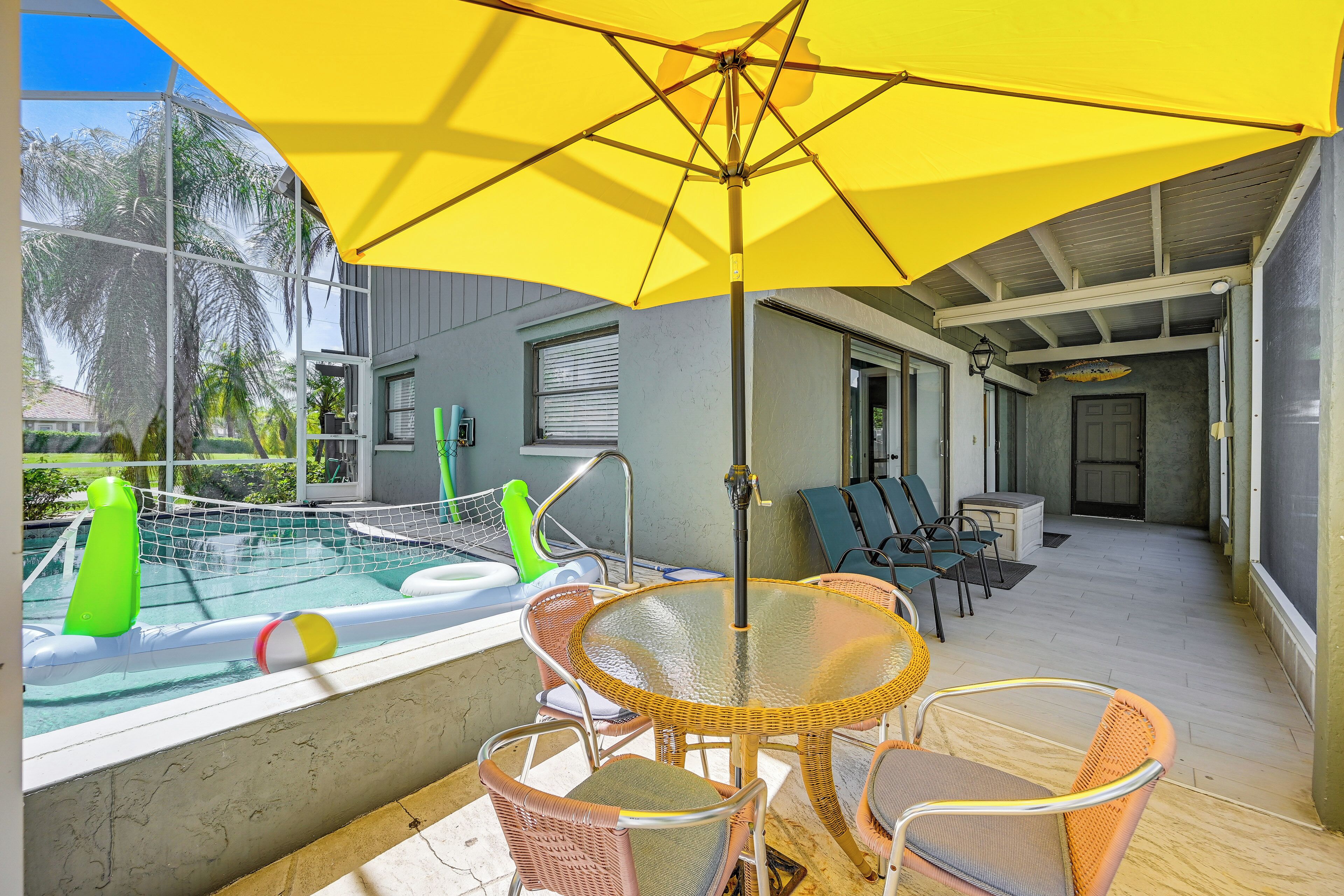 A pool area with a glass table and chairs, a yellow umbrella, and a netted pool.