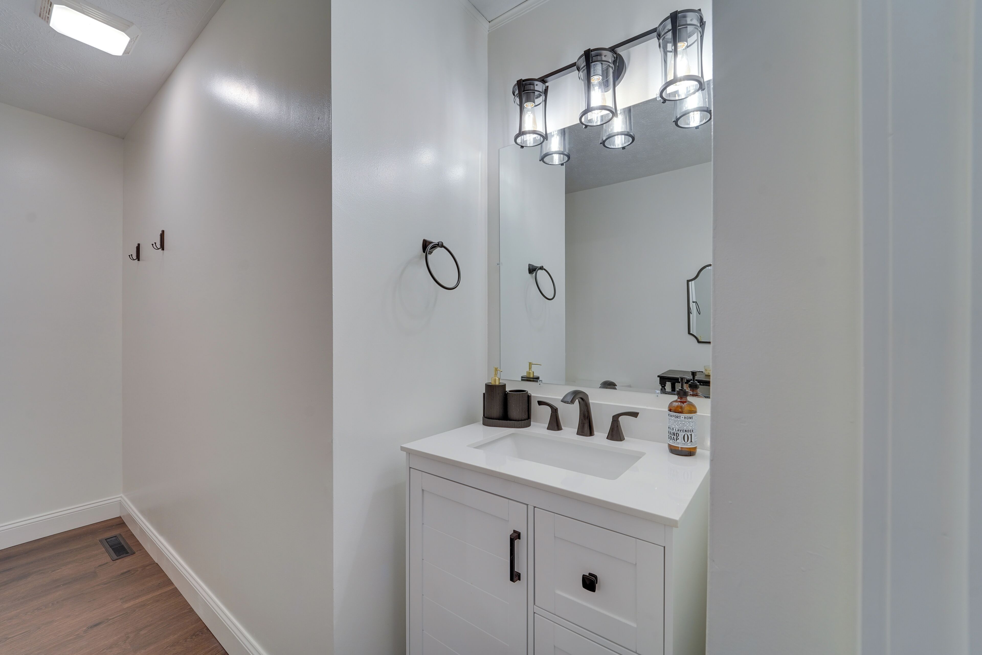 Un baño moderno con un tocador blanco, un espejo grande y tres luces fijadas a la pared.