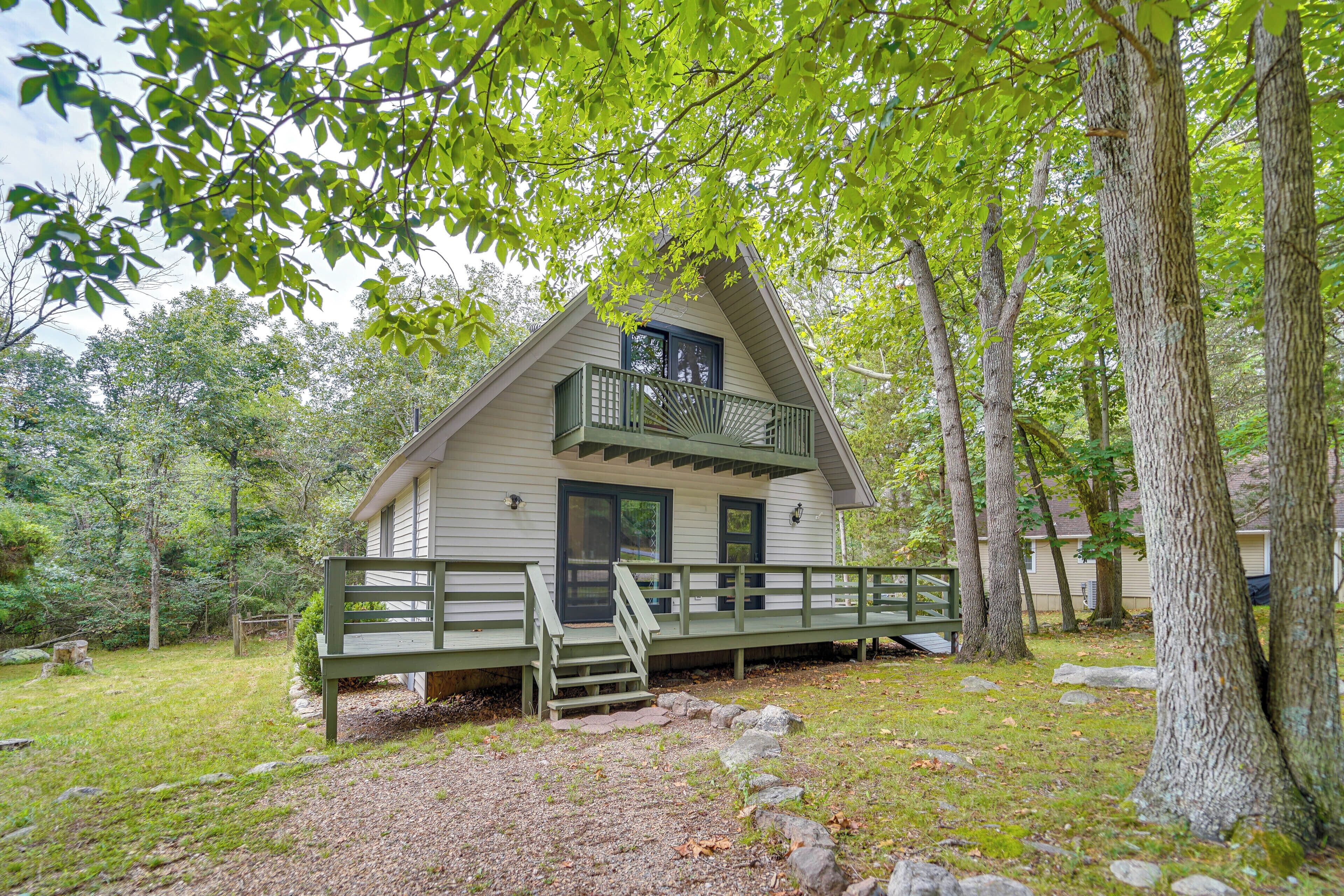 Eine Hütte mit Veranda, umgeben von Bäumen und einem grünen Rasen.