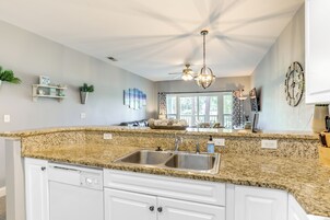 Cocina con encimeras de granito, pileta doble, muebles color blanco, ventilador de techo y decoración mural.