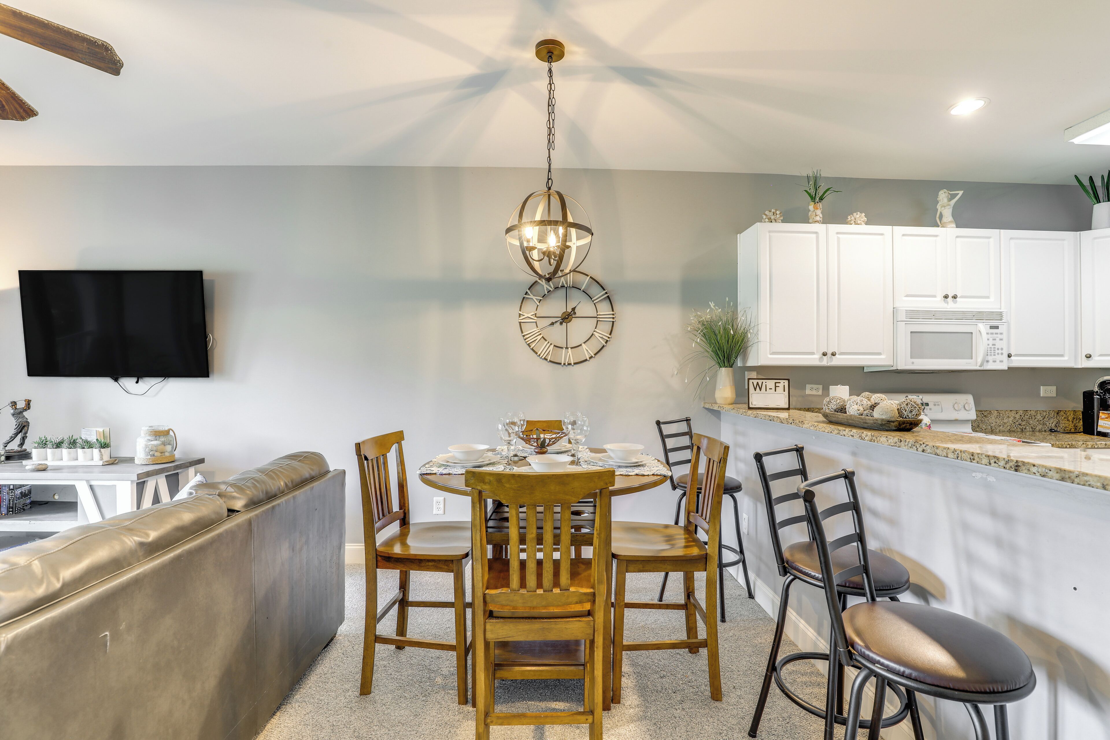 A dining area with a round table, wooden chairs, a chandelier, and white cabinets in the background.