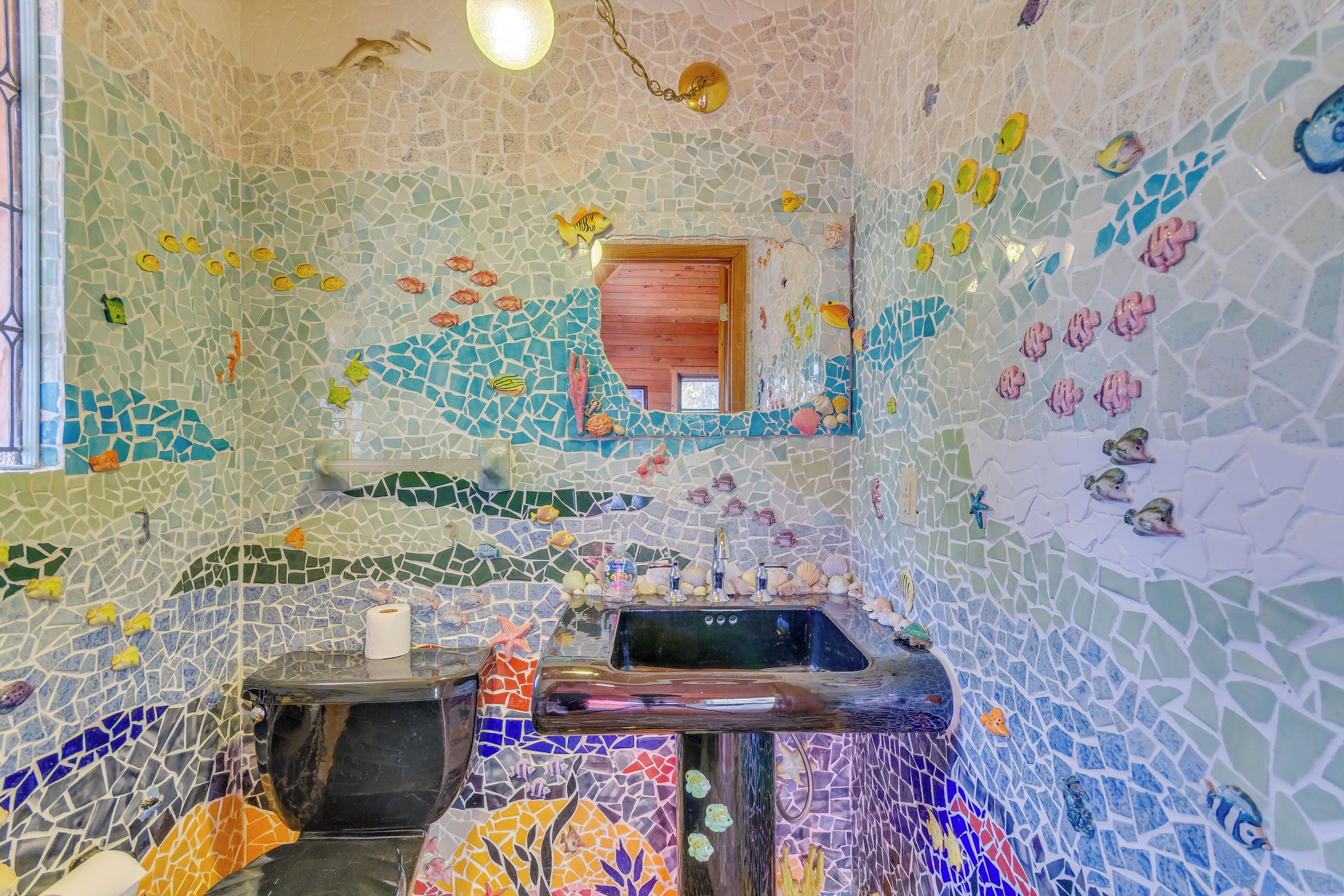 A bathroom with mosaic walls, a sink, and a toilet.