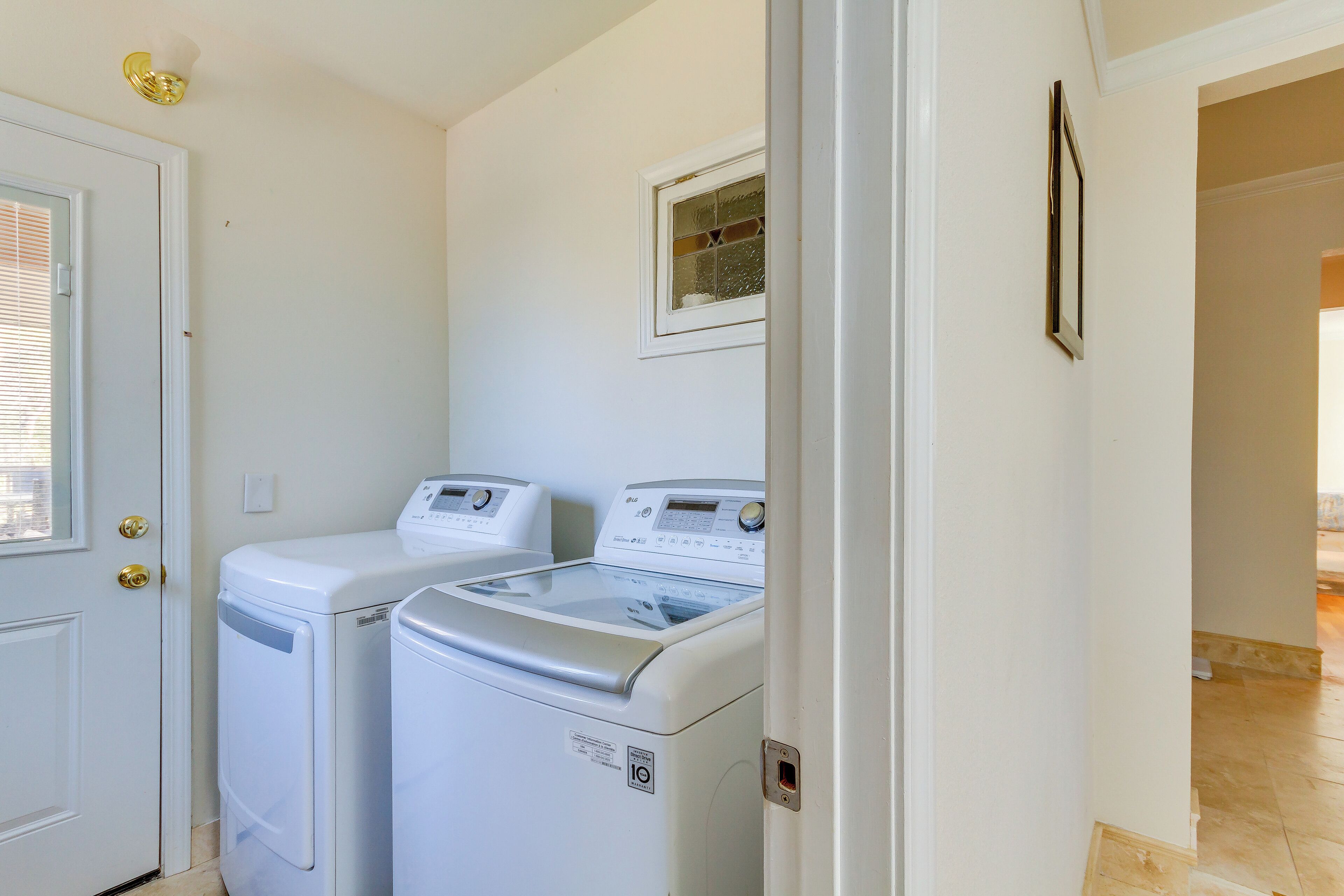 A laundry room with two white front-loading washing machines and dryers, a door with a brass handle, and a small window above the machines.