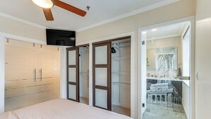 Une chambre à coucher comprenant un lit, un ventilateur de plafond, une armoire et une porte vitrée donnant sur une salle de bain.