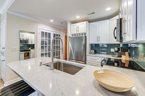 A modern kitchen with white cabinets, stainless steel appliances, a large island with a sink, and a wooden bowl. - Charming Apartment in Downtown Winston-salem! (Winston-Salem)