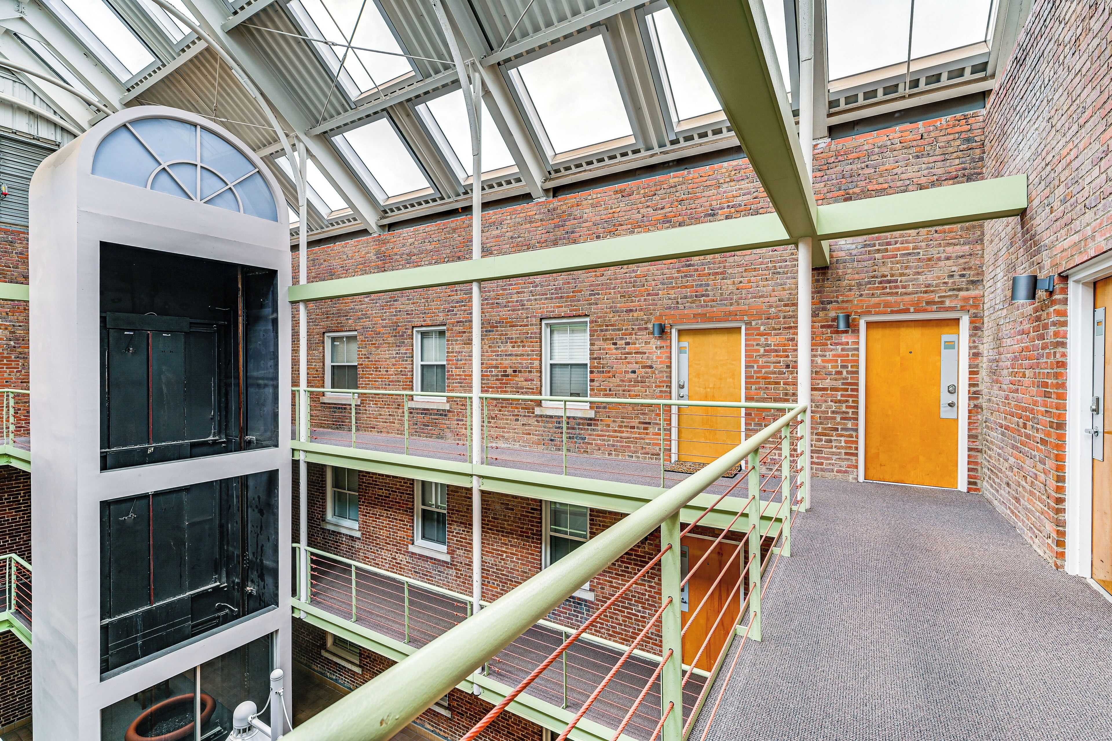 A multi-level building with a brick exterior, a glass skylight, and a staircase with a green railing.