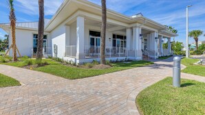 A modern building with a covered entrance, palm trees, and a brick pathway. - Pool, Golf & Beach Access: Fort Pierce Condo! (Fort Pierce)