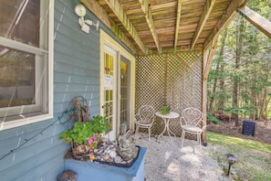 A covered porch with a wooden ceiling, a small table, two chairs, and a decorative garden bed with plants and rocks. - Cozy Boothbay Studio w/ Patio ~ 5 Mi to Harbor! (Boothbay)