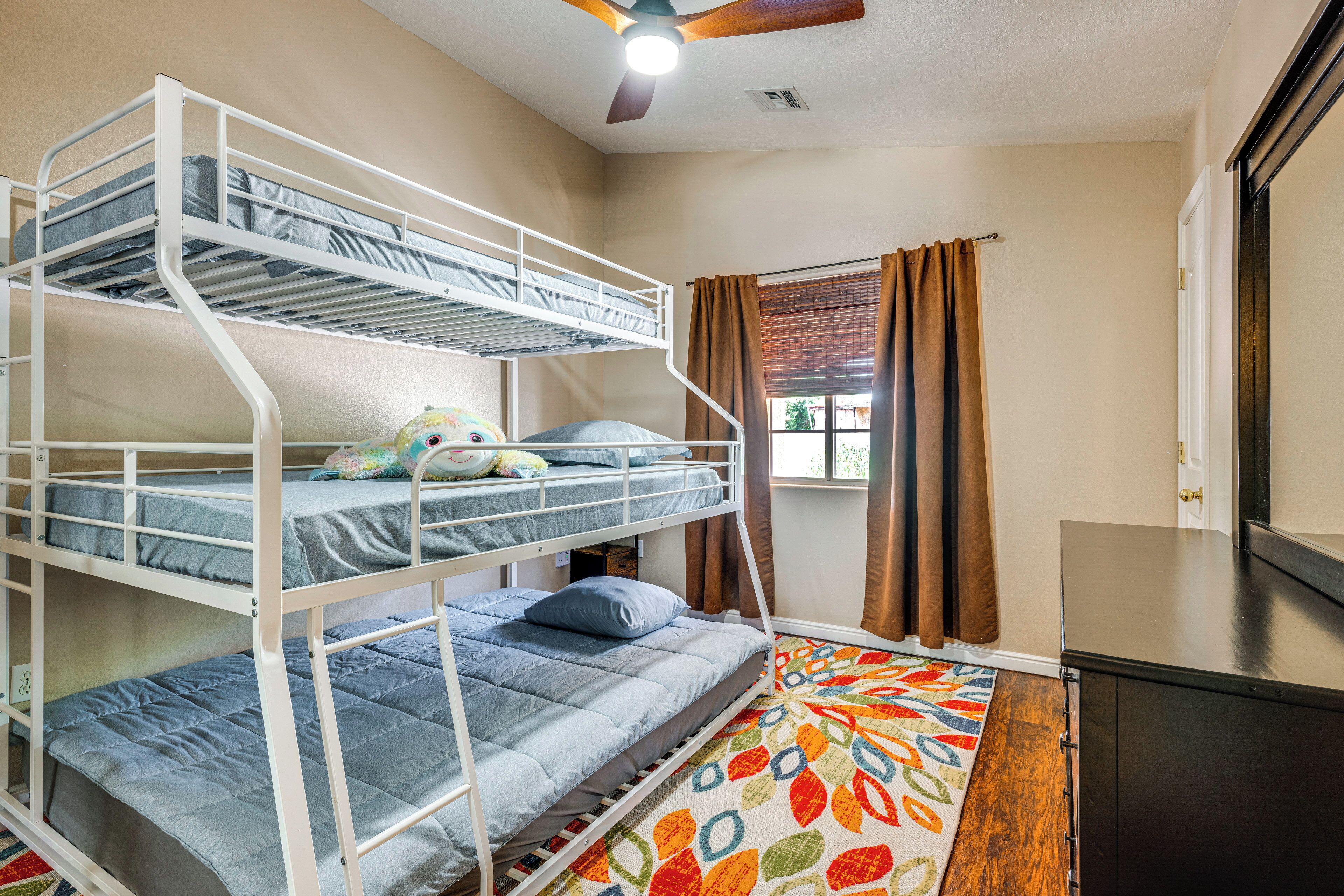 A bunk bed room with a ceiling fan, a window with curtains, and a colorful rug.